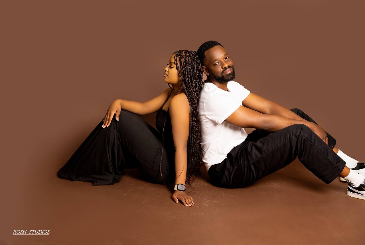 Gladman and Vongayi seated back to back on the floor of a warm brown studio