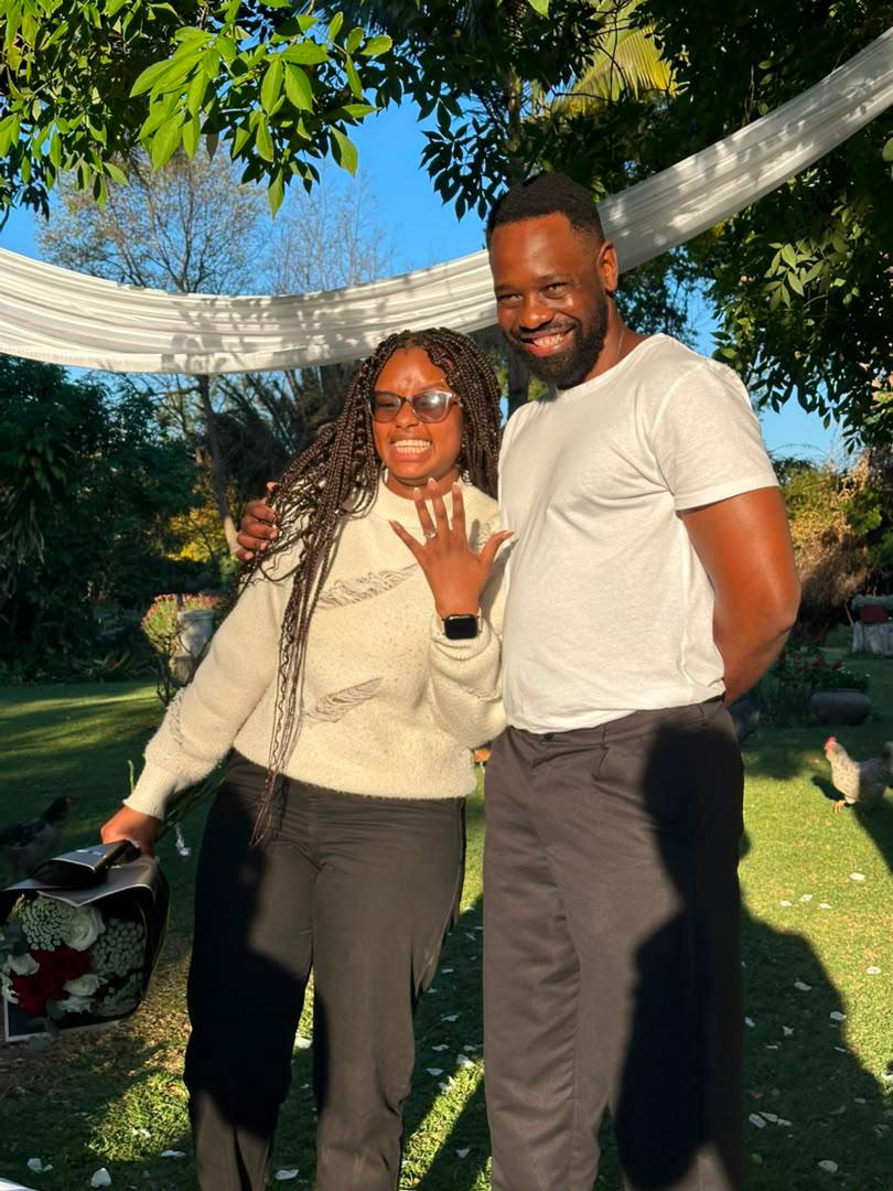 Vongayi holding up her hand to show the engagement ring, standing beside Gladman in the garden