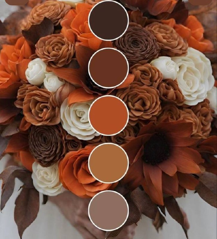 Reception table centrepiece of cream and white roses with rust-orange blooms and autumn foliage, set on a chocolate-brown tablecloth with candlelight and glassware